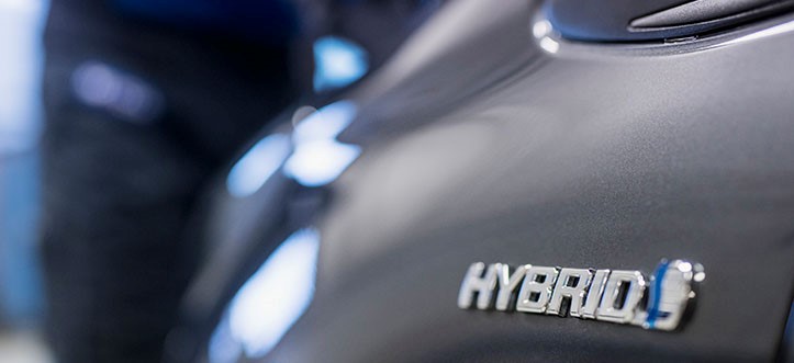 Uklart bilde av en mørkegrå bil med fokus på HYBRID-merket. Bakgrunnen er ute av fokus, men det er zoomet inn på en liten del av bilen.